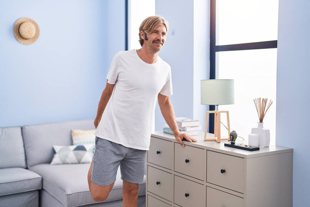 Young blond man smiling confident stretching leg at home - Photo, Image