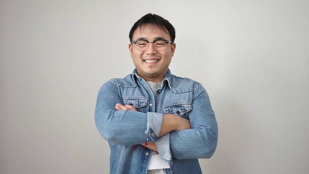Молодой китаец улыбается уверенно стоя со скрещенными руками на изолированном белом фоне - Фото, изображение