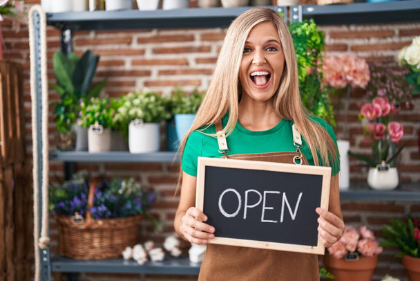 Young woman working at florist holding open sign celebrating crazy and amazed for success with open eyes screaming excited.  - Photo, Image