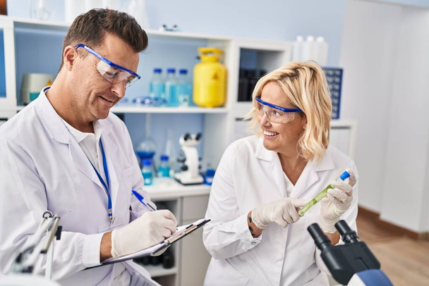 Homem e mulher de meia idade cientistas parceiros que trabalham usando microscópio e tubo de ensaio em laboratório - Foto, Imagem
