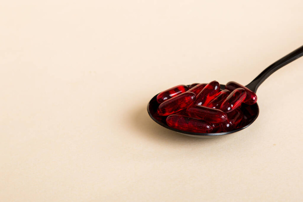 Vitamin capsules in a spoon on a colored background. Pills served as a healthy meal. Red soft gel vitamin supplement capsules on spoon. - Foto, imagen
