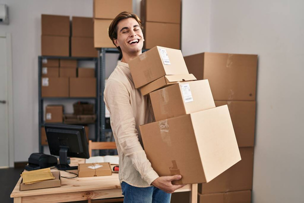 Young man working at small business ecommerce holding packages smiling and laughing hard out loud because funny crazy joke.  - Fotografie, Obrázek