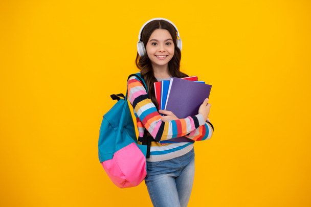 Back to school. Schoolgirl student in headphones with school bag backpack hold book on isolated studio background. School and education concept. Happy teenager, positive and smiling emotions of teen. - Photo, Image