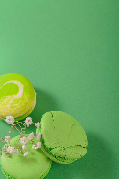 Green monochrom food background with french macaroons and flowers with copy space for text. Close up of macarons cakes from above, top view. Culinary and cooking concept - Photo, image