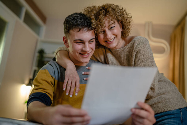 Young man male student teenager and his mother celebrate scholarship read mail letter happy exited smiling reading entry test results success celebrating achievement concept copy space real people - Fotografie, Obrázek