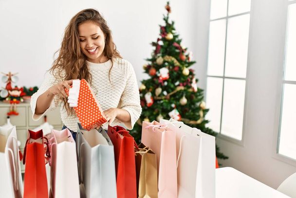 Молода красива іспаномовна жінка посміхається впевнено тримає різдвяний подарунок вдома
 - Фото, зображення