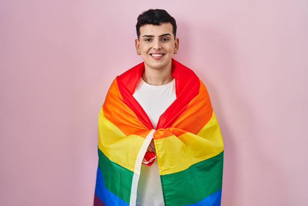Nicht binäre Person mit Regenbogen-lgbtq-Fahne sieht positiv und glücklich stehend aus und lächelt mit einem selbstbewussten Lächeln, das Zähne zeigt  - Foto, Bild