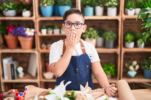 手で口を覆う花屋で働いている若いヒスパニック系の子供はショックを受け、間違いを恐れています。驚きの表情  - 写真・画像