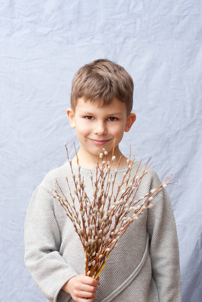 Portrait of handsome preschool boy with bouquet of spring flowers on blue background. child holding branches of flowering willow in hand, smiling. Happy easter. Palm Sunday. Springtime. - Foto, Imagen