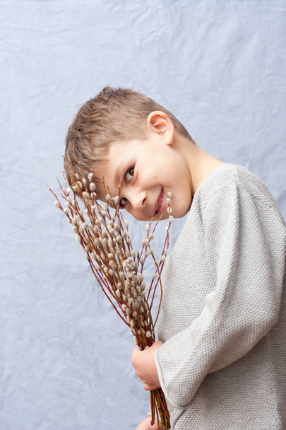Portrait of handsome preschool boy with bouquet of spring flowers on blue background. child holding branches of flowering willow in hand, smiling. Happy easter. Palm Sunday. Springtime. - Foto, immagini