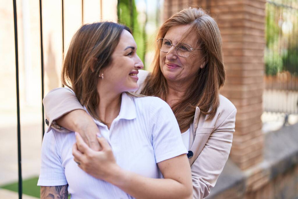 Mother and daughter smiling confident hugging each other at street - 写真・画像