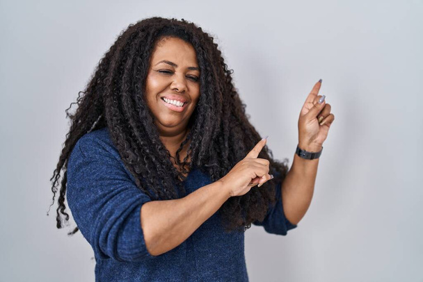 Plus size hispanic woman standing over white background smiling and looking at the camera pointing with two hands and fingers to the side.  - Фото, изображение