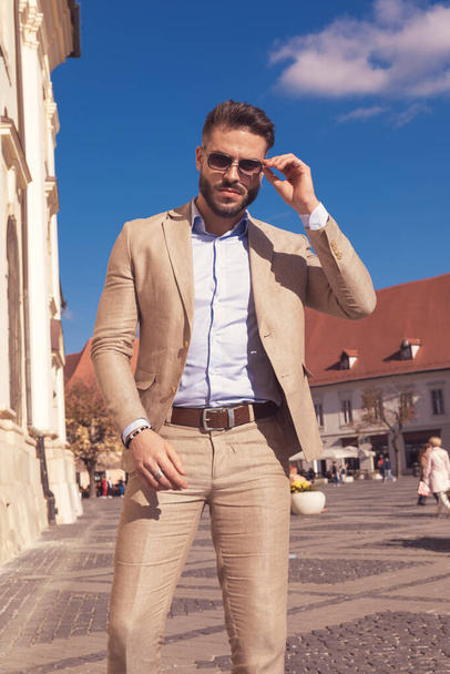 Portrait of handsome businessman arranging sunglasses and posing, wearing sunglasses outdoor, in the old medieval town - Fotografie, Obrázek