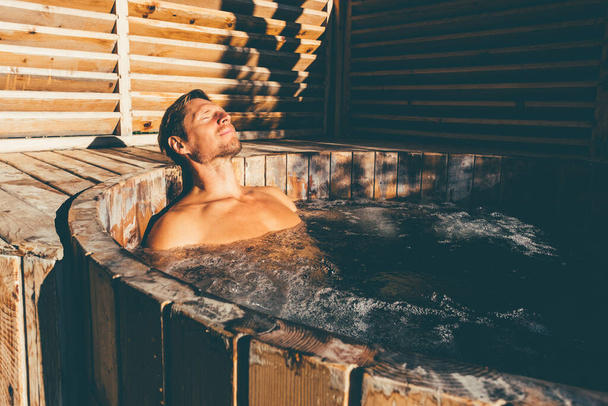 Homem relaxante na banheira de hidromassagem de madeira ao ar livre. .. Foto de alta qualidade - Foto, Imagem