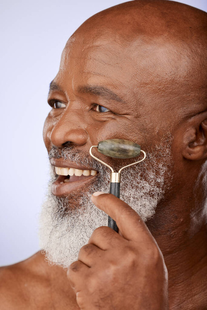 Ομορφιά, skincare και νεφρίτη ρολό προσώπου με ανώτερος άνθρωπος στο στούντιο φόντο με ένα χαμόγελο για μασάζ προσώπου με πέτρα για τη γήρανση του δέρματος πρόβλημα. Αφρικανικό μοντέλο με καλλυντικό ή δερματολογικό εργαλείο χαλαζία. - Φωτογραφία, εικόνα