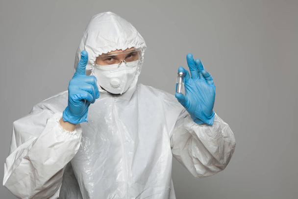 Closeup of vial to vaccinate in scientific virologist hand for immunization. Scientific virologist. Biologist in protective suit and blue gloves. Vaccination concept. - Foto, Imagen