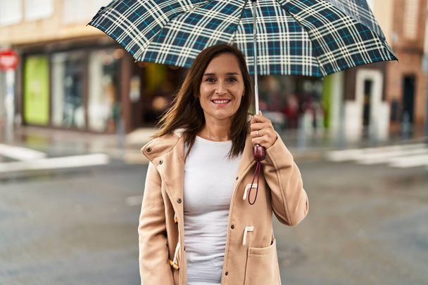 Middle age woman smiling confident using umbrella at street - Fotó, kép