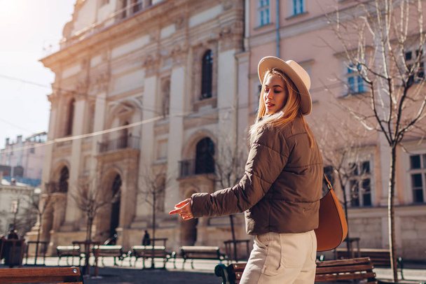 La mujer joven a la moda que camina por la calle de la ciudad europea vistiendo el sombrero elegante y la chaqueta. Moda de primavera. Ropa y accesorios beige blanco y marrón. Espacio - Foto, imagen