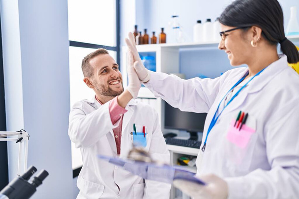 Man and woman wearing scientists uniform high five with hands raised up at laboratory - Photo, Image