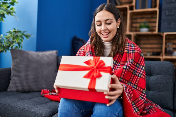 Genç İspanyol kadın hediye kutusunu açıyor çılgınlığı kutluyor ve başarıya hayret ediyor gözleri açık heyecanla haykırıyor.  - Fotoğraf, Görsel
