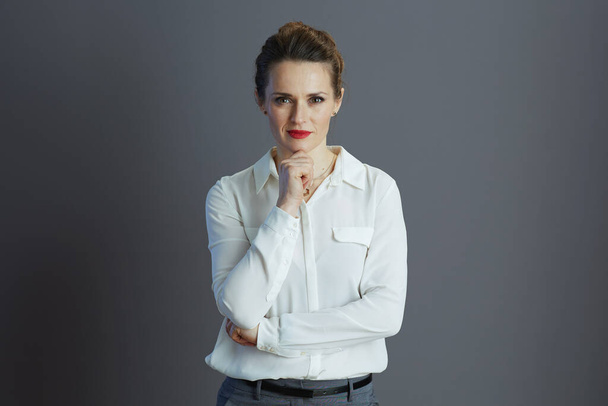 pensive modern middle aged small business owner woman in white blouse against grey background. - Fotó, kép