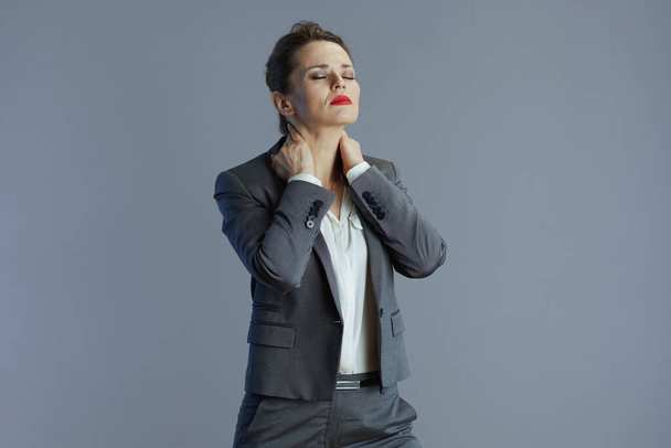 tired trendy middle aged woman worker in gray suit having neck pain isolated on gray. - Fotó, kép