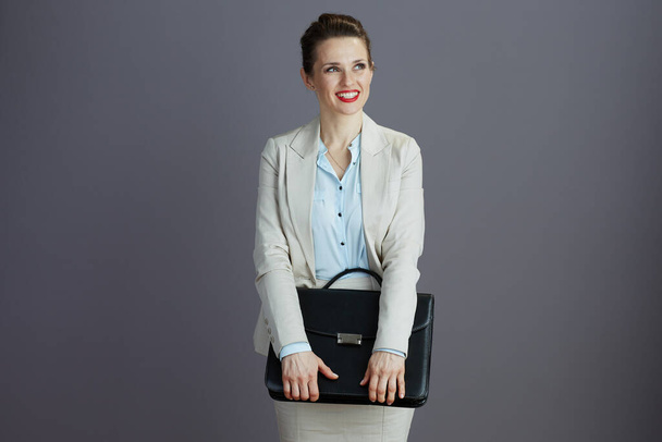 happy stylish middle aged woman employee in a light business suit with briefcase isolated on grey. - 写真・画像