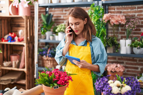Joven hermosa florista hispana hablando en smartphone usando touchpad en floristería - Foto, imagen