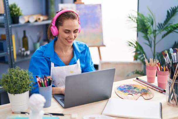 Молода жінка-художник використовує ноутбук і навушники в художній студії
 - Фото, зображення