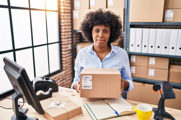 Black woman with curly hair working at small business ecommerce holding box relaxed with serious expression on face. simple and natural looking at the camera.  - Foto, imagen
