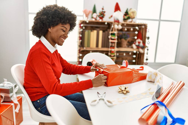 Молода афроамериканська жінка, яка посміхається, збираючи вдома подарунки з кришталевими виробами. - Фото, зображення