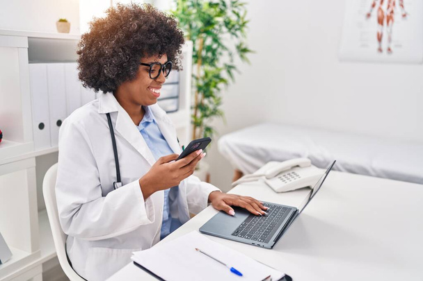 African american woman doctor using smartphone and laptop working at clinic - Photo, Image