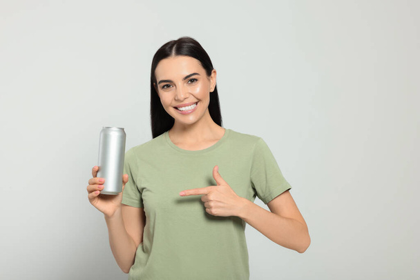 Beautiful happy woman holding beverage can on light grey background - Photo, Image