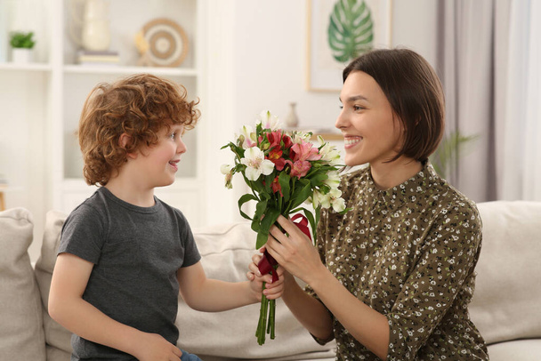 Happy woman with her cute son and bouquet of beautiful flowers at home. Mother's day celebration - Zdjęcie, obraz