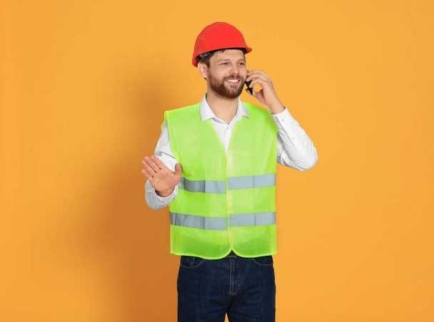 Man in reflective uniform talking on smartphone against orange background - Foto, Imagem