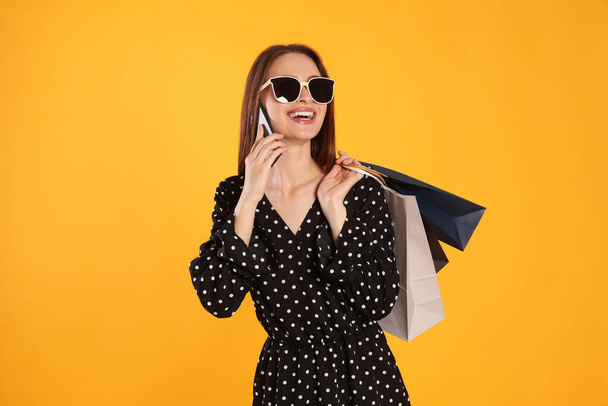Happy young woman with shopping bags and smartphone on yellow background. Big sale - Photo, image