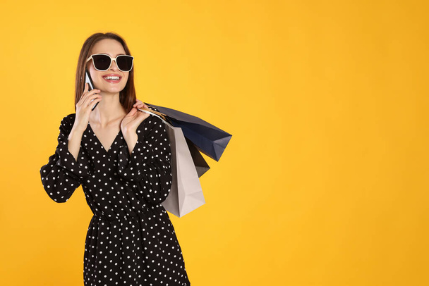 Happy young woman with shopping bags and smartphone on yellow background. Big sale - Φωτογραφία, εικόνα