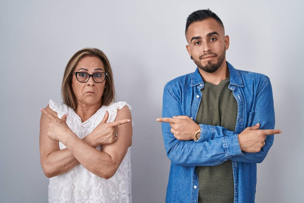 Hispanische Mutter und Sohn stehen zusammen und zeigen mit den Fingern auf beide Seiten, unterschiedliche Richtung  - Foto, Bild