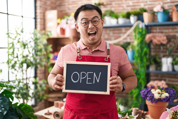Chinese young man working at florist holding open sign celebrating crazy and amazed for success with open eyes screaming excited.  - Photo, Image