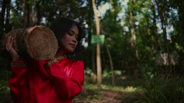 Azjatka w czerwonej bluzce, nosząca na ramionach kufer drzewa w lesie po południu. - Materiał filmowy, wideo