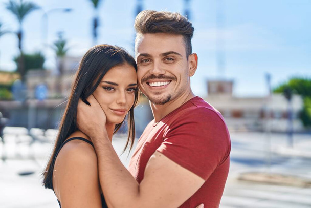man en vrouw paar glimlachen zelfverzekerd knuffelen elkaar op straat - Foto, afbeelding