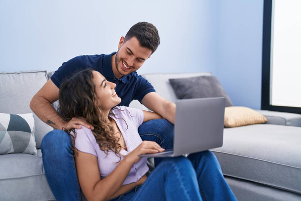 Evdeki kanepede oturan genç İspanyol çift dizüstü bilgisayar kullanıyor. - Fotoğraf, Görsel