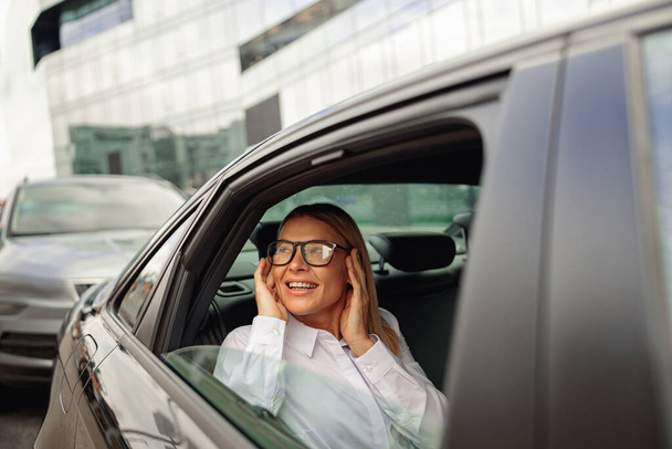 Stijlvolle zakenvrouw met een bril die met de auto reist en naar buiten kijkt. Hoge kwaliteit foto - Foto, afbeelding