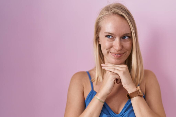 Young caucasian woman standing over pink background laughing nervous and excited with hands on chin looking to the side  - Fotó, kép