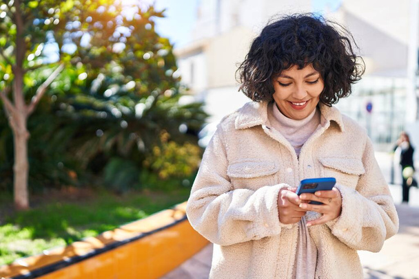 Nuori kaunis latino nainen hymyilee luottavainen käyttämällä älypuhelin puistossa - Valokuva, kuva