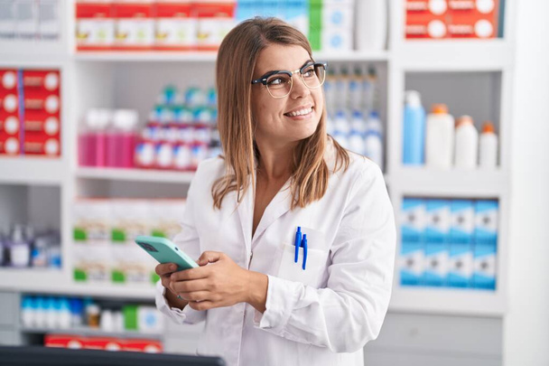 Молодая женщина-фармацевт использует смартфон, работающий в аптеке - Фото, изображение