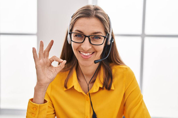 Mladá žena na sobě sluchátka agenta call centra dělat v pořádku znamení s prsty, usmívat přátelské gestikulace vynikající symbol  - Fotografie, Obrázek