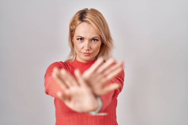 Blond vrouw staande over geïsoleerde achtergrond afwijzing expressie kruisen armen en palmen doen negatief teken, boos gezicht  - Foto, afbeelding