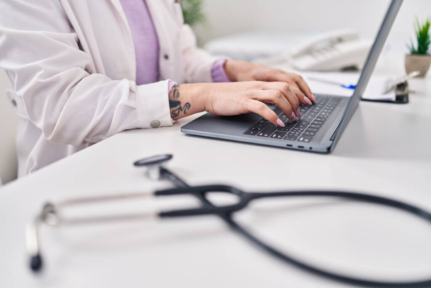 Giovane medico donna caucasica utilizzando computer portatile seduto sul tavolo in clinica - Foto, immagini