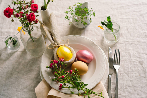 Happy Easter. Stylish easter eggs on a napkin with spring flowers on white wooden background. Table setting. The concept of a happy Easter holiday. - 写真・画像